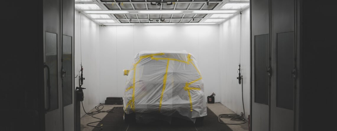 A vehicle covered with a white sheet and yellow tape in a car service garage
